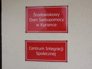 Dwie czerwone tabliczki Środowiskowy Dom Samopomocy w Kuriance oraz Centrum Integracji Społecznej.