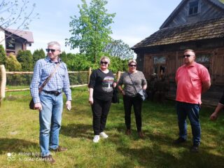 Stowarzyszenie Muzeum Małej Ojczyzny w Studziwodach. Cztery osoby stoją na trawniku przed starym drewnianym domem.