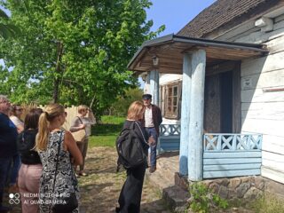 Stowarzyszenie Muzeum Małej Ojczyzny w Studziwodach. Grupa osób stoi przed wejściem do starego drewnianego domu.