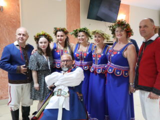 Trzecie spotkanie pt. Forum Inicjatyw Lokalnych w woj. lubelskim. Pięć uśmiechniętych kobiet z wiankami na głowach stoi w jednym rzędzie, dwójka mężczyzn z lewej i prawej oraz jeden pozujący z przodu.