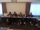 Warsztaty sieciujące na temat pracy z osobami niepełnosprawnymi intelektualnie. Kilka osób siedzi przy łączonych stołach i patrzy w jednym kierunku.