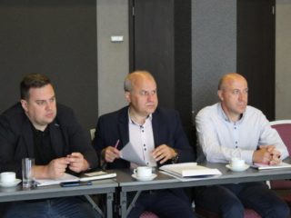 Trzech mężczyzn siedzi przy stole obok siebie.