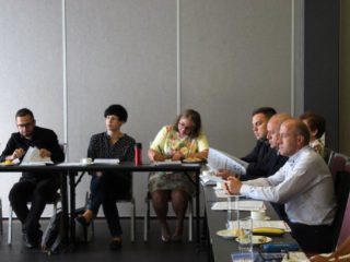 Grupa osób siedzi przy stole z dokumentami.