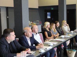 Grupa osób siedzi przy stole i patrzy w jednym kierunku.