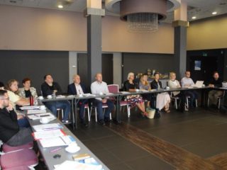 Grupa ludzi siedzi przy stole i patrzy w jednym kierunku.