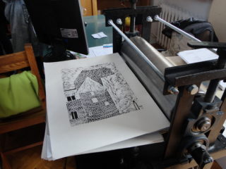Czarnobiały rysunek ceglanej wieży leży obok żelaznej maszyny z wałkami. Obok stanowisko z monitorem i dokumentami.
