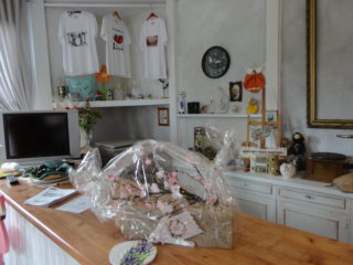 Jasne pomieszczenie z różnymi przedmiotami m.in. koszulki, figurki, kwiaty.