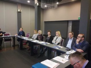 Grupa osób siedzi przy stole i patrzy w jednym kierunku.