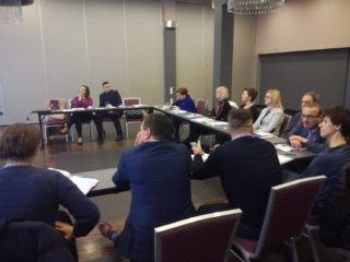 Grupa osób siedzi przy stole podczas spotkania.