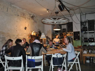 Stare pomieszczenie z obdartymi ścianami, z nowoczesnym wyposażeniem oraz ludźmi którzy jedzą przy stole.