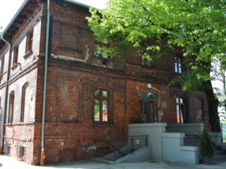 Budynek z czerwonej cegły z odrestaurowanym wejściem i zielonym drzewem rosnącym przy wejściu.