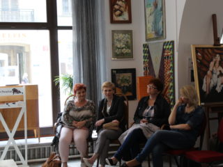 Cztery kobiety siedzą w pomieszczeniu z obrazami.