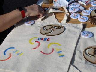 Stół z broszkami, drewnianymi szablonami i torbami z namalowanymi logotypami Podlaskich Targów Ekonomii Społecznej.