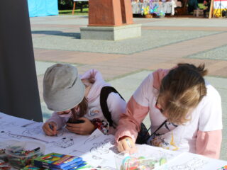 Dwójka dzieci siedzi przy stoisku i koloruje kolorowanki.