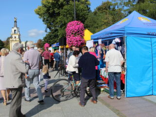 Grupa osób zgromadzona przy stoiskach które stoją w jednym rzędzie.