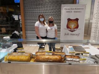 Dwie kobiety w maseczkach stoją za stoiskiem z mięsnymi potrawami. Obok stoi tablica - Polski Dom Rodzinny Serce - Sokółka.