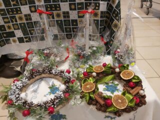 Trzy świeczki w foli ozdobione gałązkami i szyszkami oraz dwa wieńce świąteczne zrobione z martwej natury typu szyszki, cytryny, gałązki.