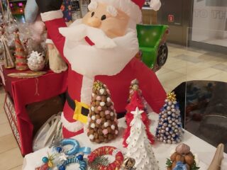 Dmuchany święty Mikołaj przy stole z małymi choinkami zrobionymi z martwej natury.