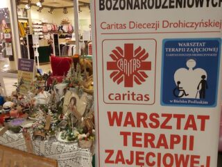 Baner - Kiermasz ozdób bożonarodzeniowych. Obok stoi stoisko z ozdobami świątecznymi.