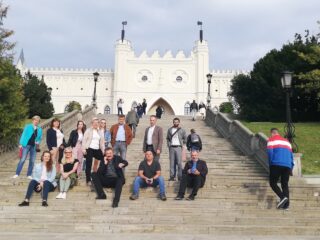 Grupowe zdjęcie na schodach prowadzących do zamku królewskiego w Lublinie. Kilka osób siedzi na schodach.