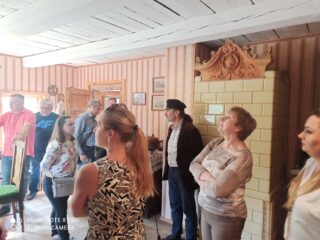 Stowarzyszenie Muzeum Małej Ojczyzny w Studziwodach. Grupa osób chodzi i rozgląda się po starym domu z piecem kaflowym.